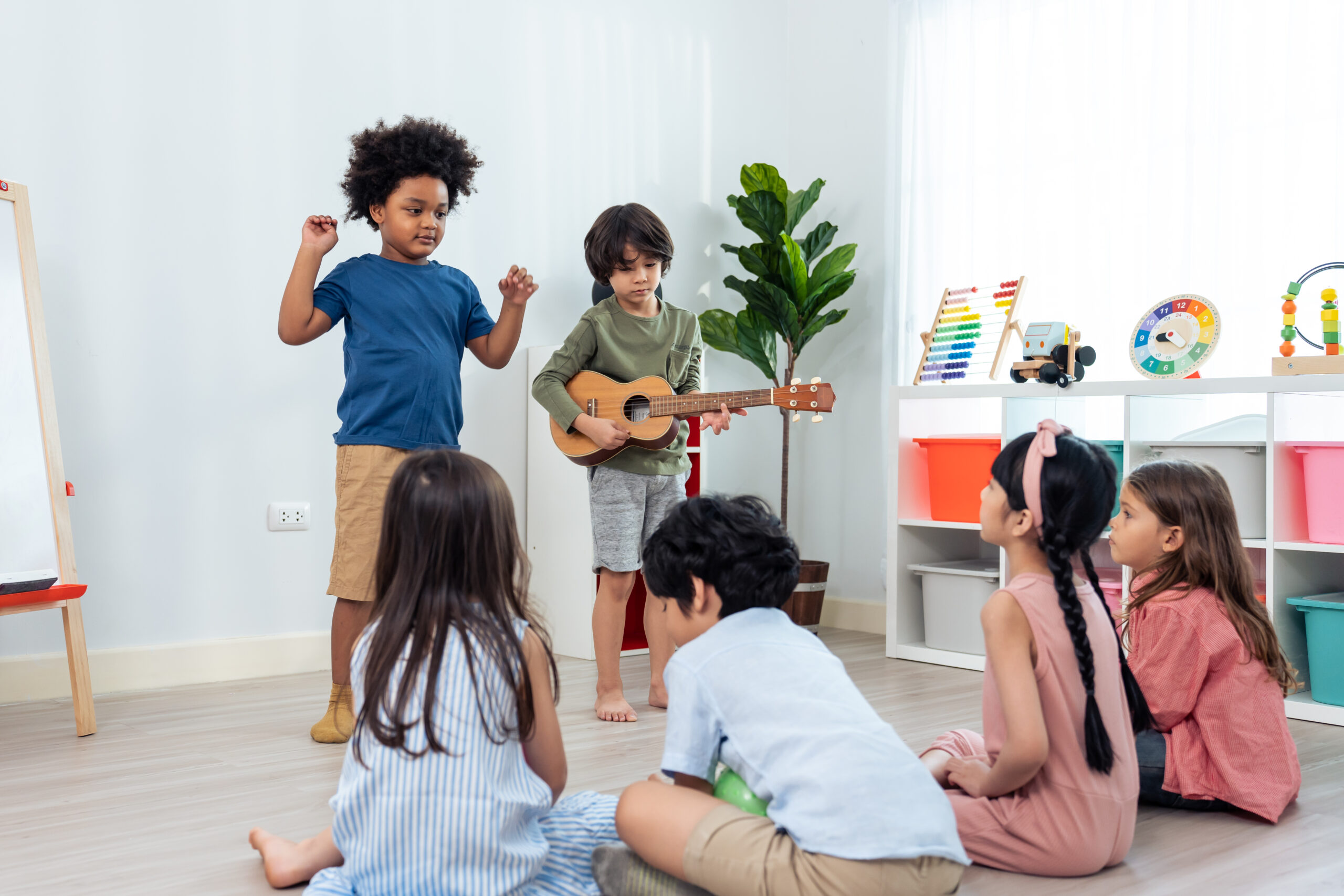 Group of Mixed race young little kid playing guitar in schoolroom. Child girl and boy student spend time play music sing a song and dancing while break with feeling fun together in classroom at schoo